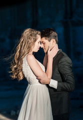 Closeup Portrait of wedding bride and groom with bouquet posing by the old cathedral. Bridal couple, Happy Newlywed woman and man hugging. Bride and groom