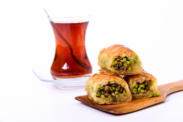 Traditional Turkish Dessert, Baklava on the wooden plate with pistachio nuts and Turkish Tea with spoon on the white surface.