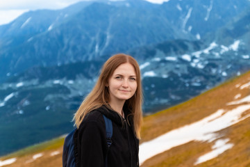 Naklejka premium A cute blonde girl in a warm gray sweater climbed the peak of the mountain and looks at the photographer s camera. Travel day concept. Tourist adventures