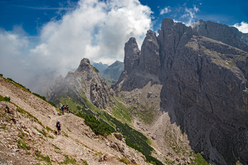 Fototapeta premium Some hikers go along an impassable rocky path, in view of the towers and peaks of the Friulian Dolomites, in Italy.