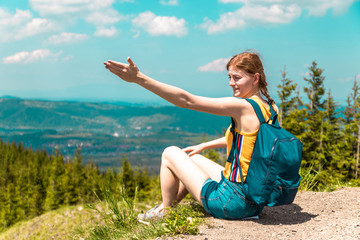 Outraged tired girl with a backpack sits on a mountain and enjoys the beautiful hills of the mountain on a sunny day.