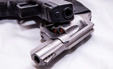Two handguns, a silver snub nosed 357 magnum revolver and a black 9mm pistol on a white background