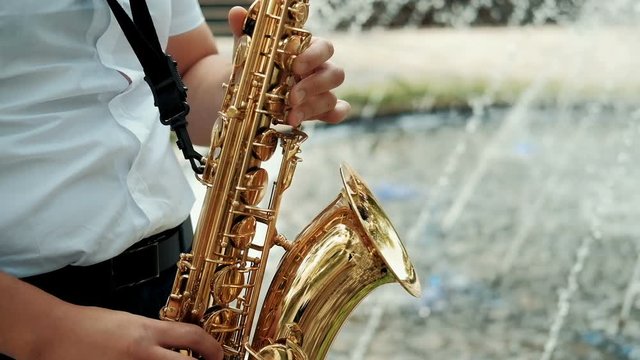 Close up of male's hands playing the saxophone. Man plays the saxophone in the park at the fountain.