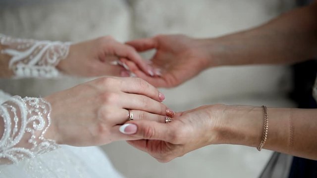 The bride and her mom hold hands. The daughter puts her hands in the hands of her mother.