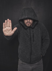 Mystery unknown man in hood with stop gesture on dark