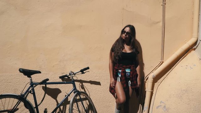 Portrait of the cute attractive young girl standing on the yellow wall next to the bike