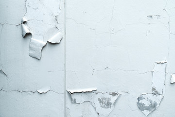 The old white concrete wall with cracks and sheet peeling of paint.