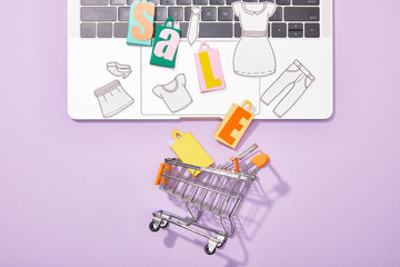 top view of small paper bags with sale lettering and paper cut of clothes on laptop falling in toy...