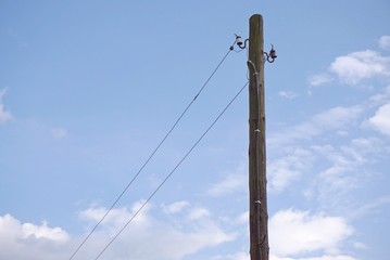 Wooden post with cables a blue sky background. Old electric pole in the countryside