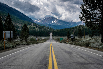 A wide open road leading to stormy, snow covered mountains