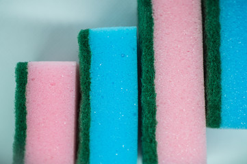 Different color sponges for washing dishes, staggered on top of each other close up on a white background