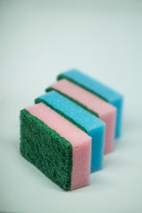 Different color sponges for washing dishes, staggered on top of each other close up on a white background