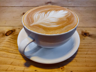 Cappuccino with leaf like art and golden glitters served in a white cup. Top view