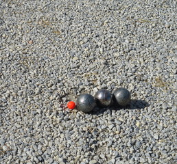 oules de pétanques alignées et cochonnet rouge sur gravier blanc.