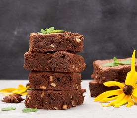 stack of square baked pieces of brownie chocolate cake with walnuts on the table