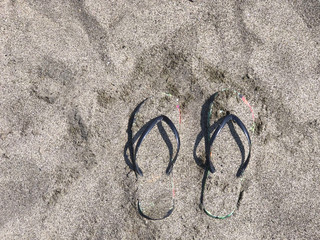 Fototapeta na wymiar Flip-flops covered with sand on beach