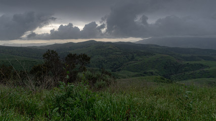 From the top of a hill looking at an approaching storm blanketing an open landscape of hills and valleys