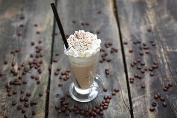 Iced coffee, glass of coffee with milk, whipped cream and ice on a wooden background.