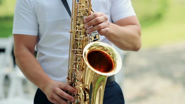 Closeup, of male's hands playing the saxophone outdoors.
