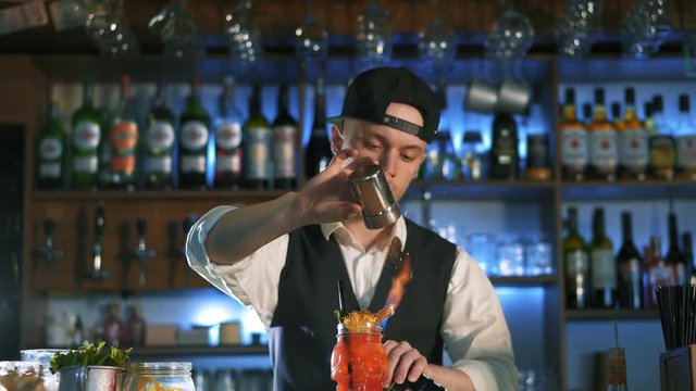 The bartender is preparing an alcoholic cocktail. He sets fire to cinnamon