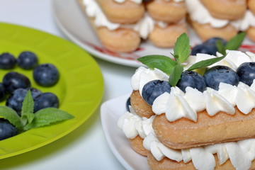 Making a cake of Italian savoiardi cookies and cream. Nearby is a plate with blueberries and mint leaves to decorate cakes.