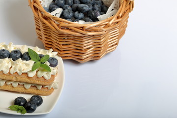 Cakes made from Italian savoyardi cookies and cream. Decorated with blueberries and mint leaves. Fresh blueberries are collected in a wicker basket.