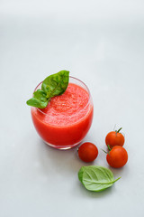 Glass of freshly squeezed tomato juice with cherry tomatoes and basil leaves on gray background. Healthy food concept. Copy space