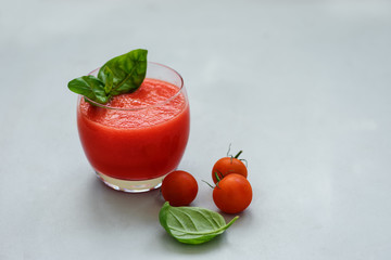 Glass of freshly squeezed tomato juice with cherry tomatoes and basil leaves on gray background....