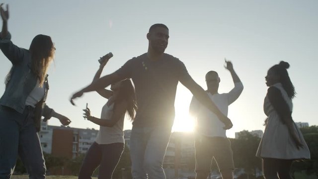 Smiling handsome young man spinning while dancing. Group of happy young people dancing in park. Dancing concept