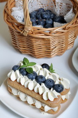 Cakes made from Italian savoyardi cookies and cream. Decorated with blueberries and mint leaves. Fresh blueberries are collected in a wicker basket.
