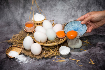 Woman hands breaking an egg to separate egg white and yolks and egg shells at the background