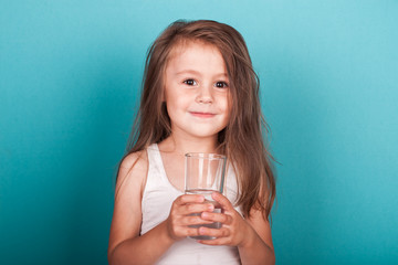 Cute little girl drinking water from glass on blue background