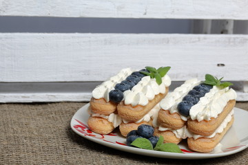 Cakes made from Italian savoyardi cookies and cream. Decorated with blueberries and mint leaves. Nearby is a box of white painted wooden boards.