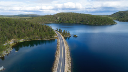 Fototapeta na wymiar Aerial view of unlimited space of forest plain, highway and lakes. Asphalt road between green fir and pine trees under cloudy sky. Perspective view, summer season in Lapland.