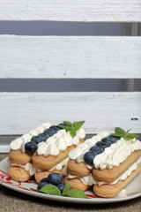 Cakes made from Italian savoyardi cookies and cream. Decorated with blueberries and mint leaves. Nearby is a box of white painted wooden boards.