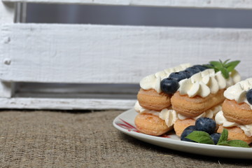 Cakes made from Italian savoyardi cookies and cream. Decorated with blueberries and mint leaves. Nearby is a box of white painted wooden boards.