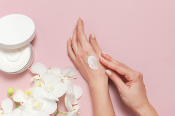 Young woman moisturizes her hand with cosmetic cream lotion opened container with cream body milk...