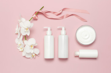 Fototapeta na wymiar Beauty Spa concept. Opened container with cream, cosmetic bottle containers, white Phalaenopsis orchid flowers on pink background Flat lay top view. Herbal dermatology cosmetic hygienic cream