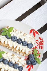 Cakes made from Italian savoyardi cookies and cream. Decorated with blueberries and mint leaves. They stand on a box of white painted wooden boards.