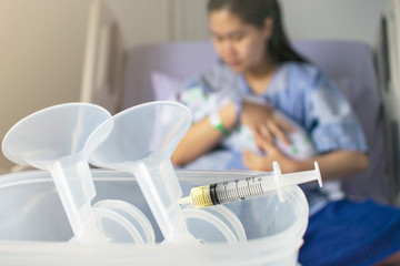 Mother holding a baby syringe with breast milk for breastfeeding at foreground, mothers breast milk is the most healthy food for newborn baby.