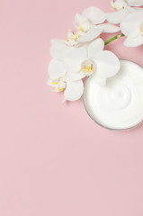 Obraz na płótnie Canvas Beauty Spa concept. Opened plastic container with cream and White Phalaenopsis orchid flowers on pink background Flat lay top view. Herbal dermatology cosmetic hygienic cream, organic cosmetic Natural