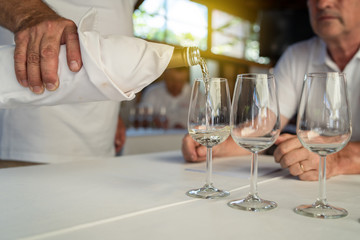 Man sommelier waiter pouring wine in the drinking glass at the testing ceremony event for the expert to test it and give marks about the quality to the degustation card