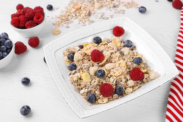 bowl of oat granola, muesli with fresh raspberries, blueberries on white wooden board for healthy breakfast. top view