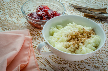 A tasty looking dish of rice pudding with a small bowl of strawberry jam and cinnamon. 