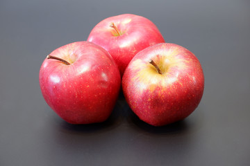 Three juicy ripe apples in group on dark gray background close up view