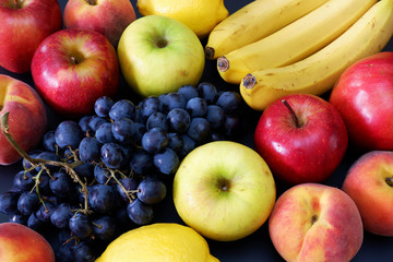 Naklejka na ściany i meble Fresh juicy fruits: bananas, black vine grapes, red apples, peaches, lemons on black background