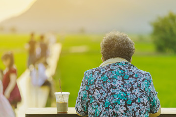 Back view of senior woman sit for resting and waiting for time to take photos of the sunset on the farmer's balcony in the rice fields.