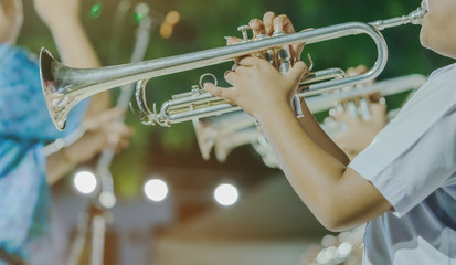Male student with friends blow the trumpet with the band for performance on stage at night.