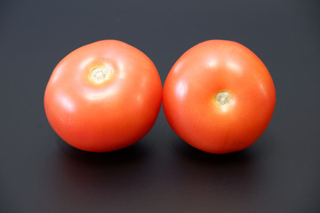 Two ripe juicy red tomatoes on dark gray background close up