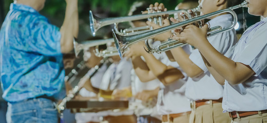 Male student with friends blow the trumpet with the band for performance on stage at night.